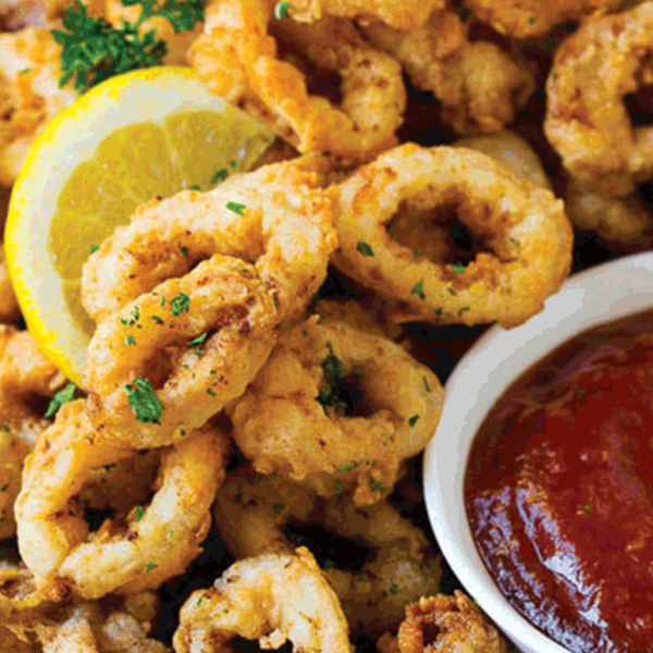 Photo of calamari with lemon wedge and red dipping sauce.